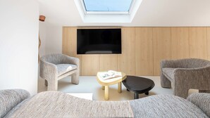 A modern living room with a skylight, a flat-screen TV, and two wicker chairs.