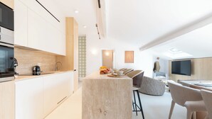 A modern kitchen with a central island, a dining area with a high table and chairs, and a living space with a sofa and TV.