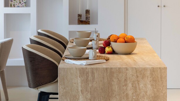 A modern kitchen with a marble countertop, a bowl of fruit, and a set of bowls and cups.