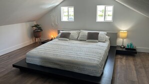 A bedroom with a sloped ceiling, a bed with patterned bedding, a bedside table with a lamp, and a potted plant.