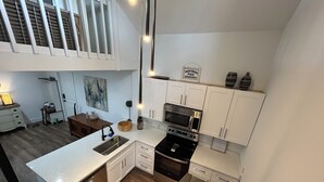 A modern kitchen with white cabinets, a stainless steel sink, a microwave, and a stove.