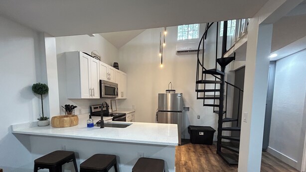 A modern kitchen with white cabinets, a stainless steel refrigerator, a microwave, and a black spiral staircase.