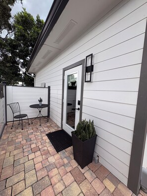 A patio with a table and chairs, a potted plant, and a door leading to an interior space. - Cozy 1-Bedroom Loft Apartment in the Heart of Fort Myers! (Fort Myers)