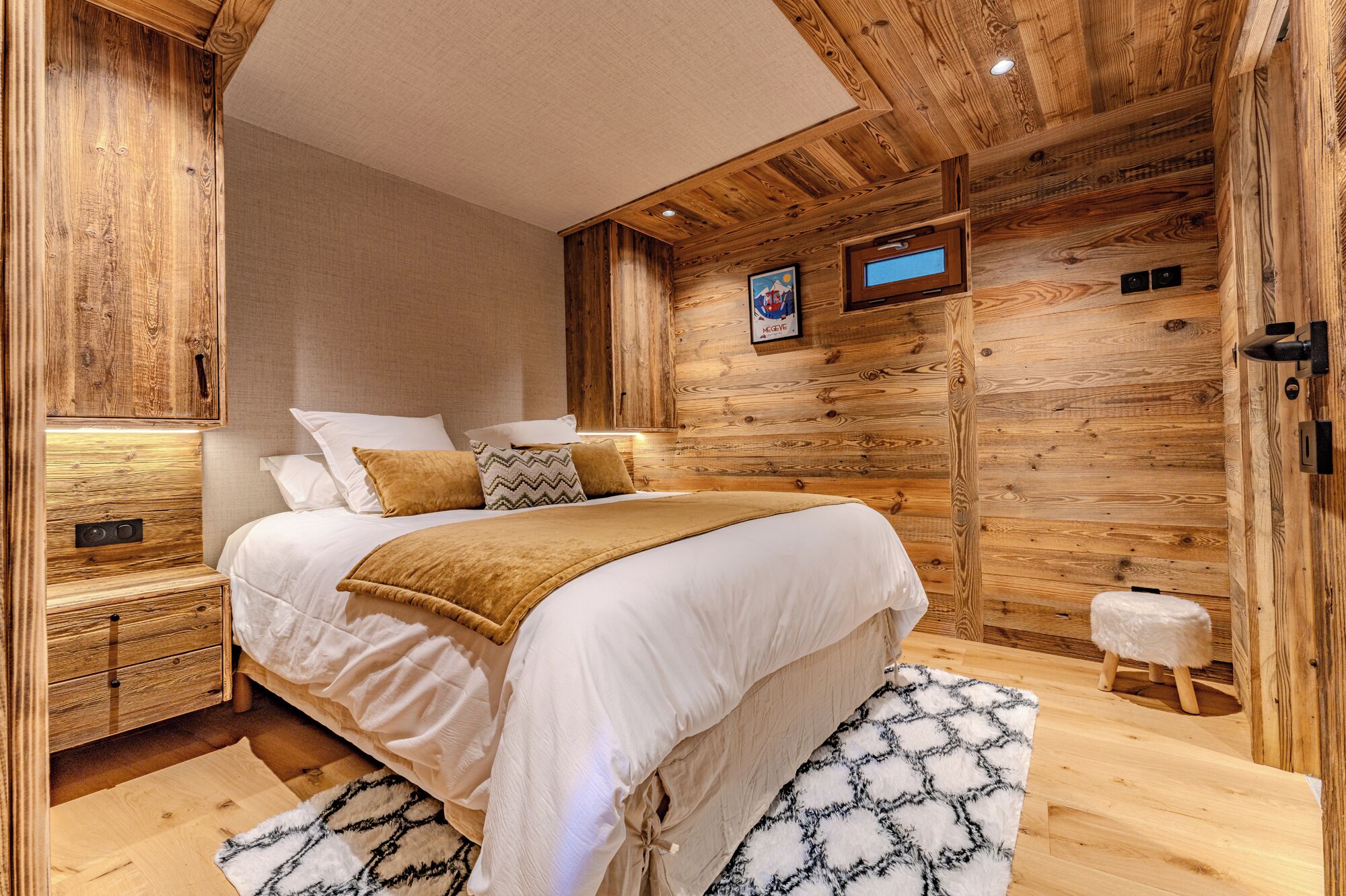 Une chambre confortable avec un plafond en bois, un lit recouvert de linge de lit blanc, une petite table de chevet et un tapis moelleux.