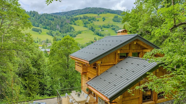 Une cabane en bois dotée d’un bain à remous et d’un espace extérieur aménagé, entourée d’une végétation luxuriante et offrant une vue sur des collines ondulantes.