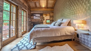 Une chambre confortable avec un grand lit, une fenêtre à carreaux, un plafond en bois et un mur orné de motifs.