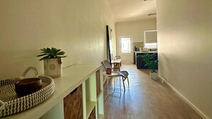Un pasillo con piso de madera, pared blanca, una pequeña mesa con una planta y una silla.