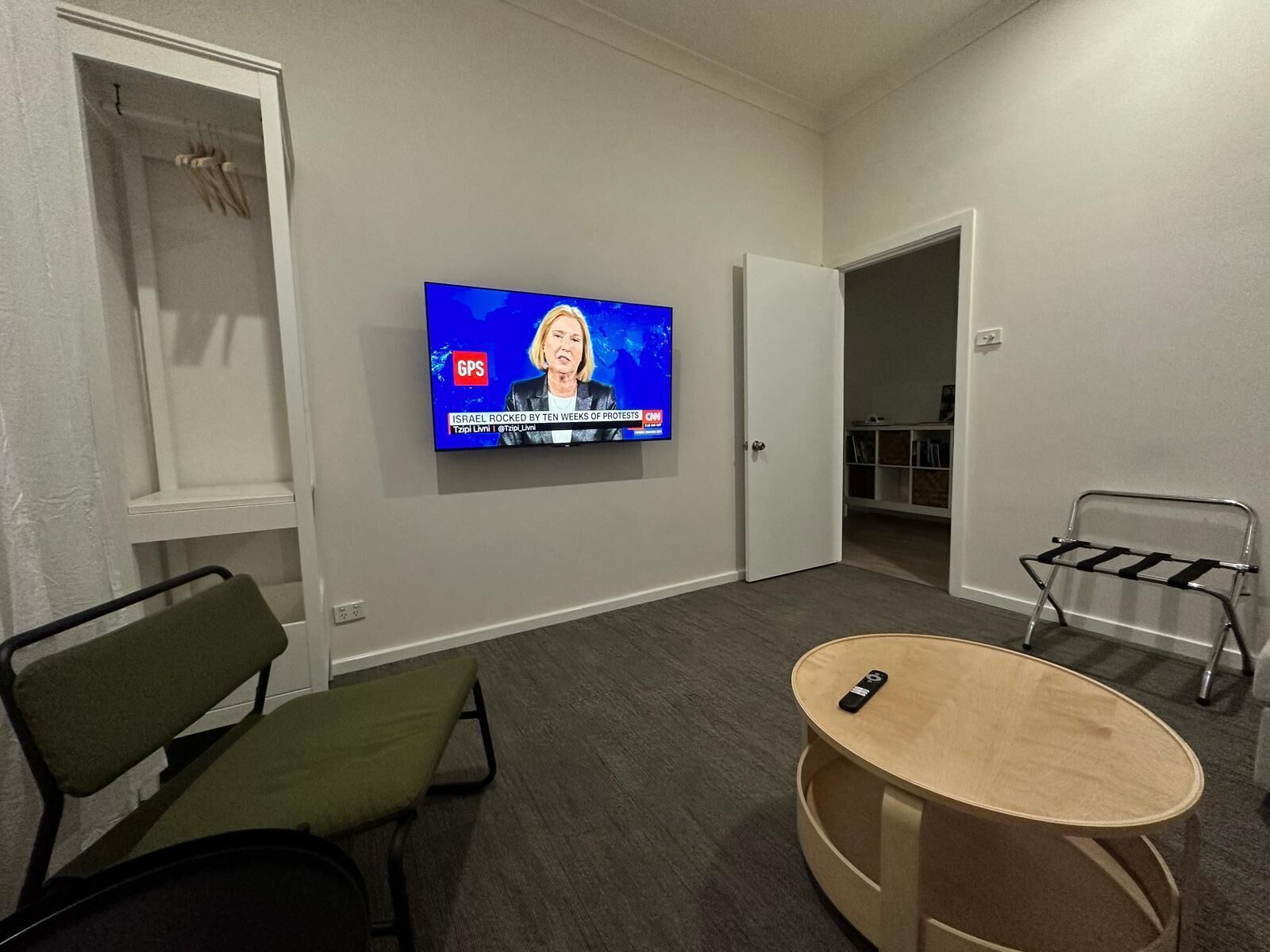 A modern living room with a flat-screen TV mounted on the wall, a green chair, a wooden coffee table, and a metal side table.