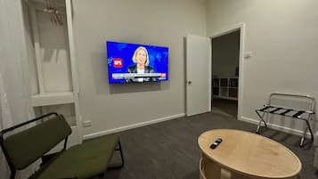 A modern living room with a flat-screen TV mounted on the wall, a green chair, a wooden coffee table, and a metal side table.