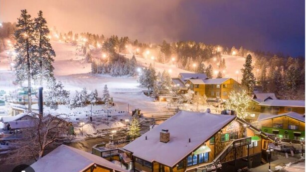 Een besneeuwd dorp met houten huizen, een piste in de verte en een klein riviertje op de voorgrond.