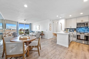 A modern kitchen with white cabinetry, a central island, and a dining area with a round table and chairs.