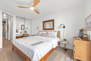 Une chambre à coucher comprenant un lit, des tables de chevet, un miroir, un ventilateur de plafond et une petite table ronde avec une lampe.