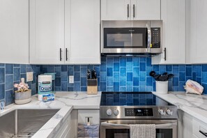 A modern kitchen with white cabinets, a stainless steel microwave, a gas stove, and blue-tiled backsplash.