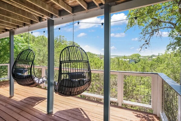 A wooden deck with hanging black chairs and a white railing overlooking a green landscape. - Hillside Hacienda with a view and a hot tub! (Canyon Lake)