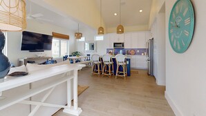A spacious kitchen with white cabinets, a large clock, and a dining area with wicker chairs. - Beach Access, Private Hot Tub, Shared Pool (Port Aransas)