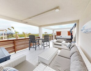 A covered outdoor patio with a hot tub, seating area, and a view of the beach.