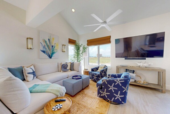 A modern living room with a large sofa, two armchairs, a coffee table, and a TV mounted on the wall.
