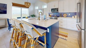 A modern kitchen with a central island, bar stools, a microwave, and a refrigerator. - Beach Access, Private Hot Tub, Shared Pool (Port Aransas)