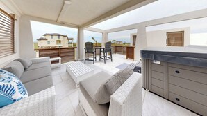 A covered outdoor seating area with a sofa, chairs, and a grill. - Beach Access, Private Hot Tub, Pet Friendly, Shared Pool (Port Aransas)