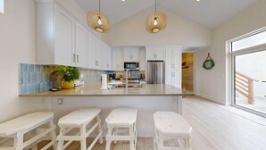 A modern kitchen with white cabinets, a central island with stools, a microwave, a refrigerator, and pendant lights. - Beach Access, Private Hot Tub, Pet Friendly, Shared Pool (Port Aransas)