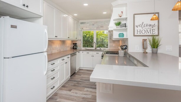 A modern kitchen with white cabinetry, a central island, and a welcoming sign. - Steps from Sand * New Remodel * BBQ (San Diego)