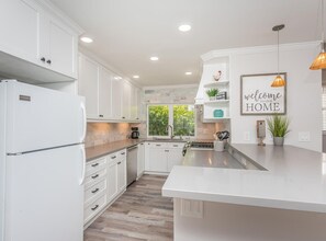 Une cuisine moderne avec des meubles blancs, un îlot central et une pancarte accueillante.