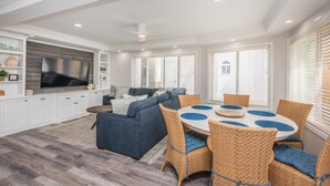 A spacious living area with a large flat-screen TV, a dark blue sofa, and a round dining table with wicker chairs. - Steps from Sand * New Remodel * BBQ (San Diego)