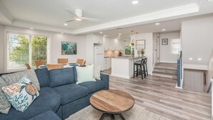A modern living room with a blue sofa, a wooden coffee table, and a dining area with a round table. - Steps from Sand * New Remodel * BBQ (San Diego)