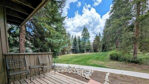 A wooden deck with metal chairs and a small table, surrounded by a garden with a stone border and a lawn. - Flying Dutchman 1155 (Keystone)