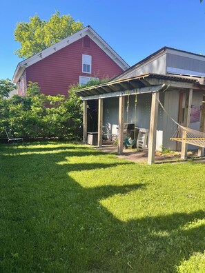 A covered patio area with a hammock, a wooden deck, and a red barn in the background. - 5BR Retreat on Battery Park, Sleeps 10 (Burlington)