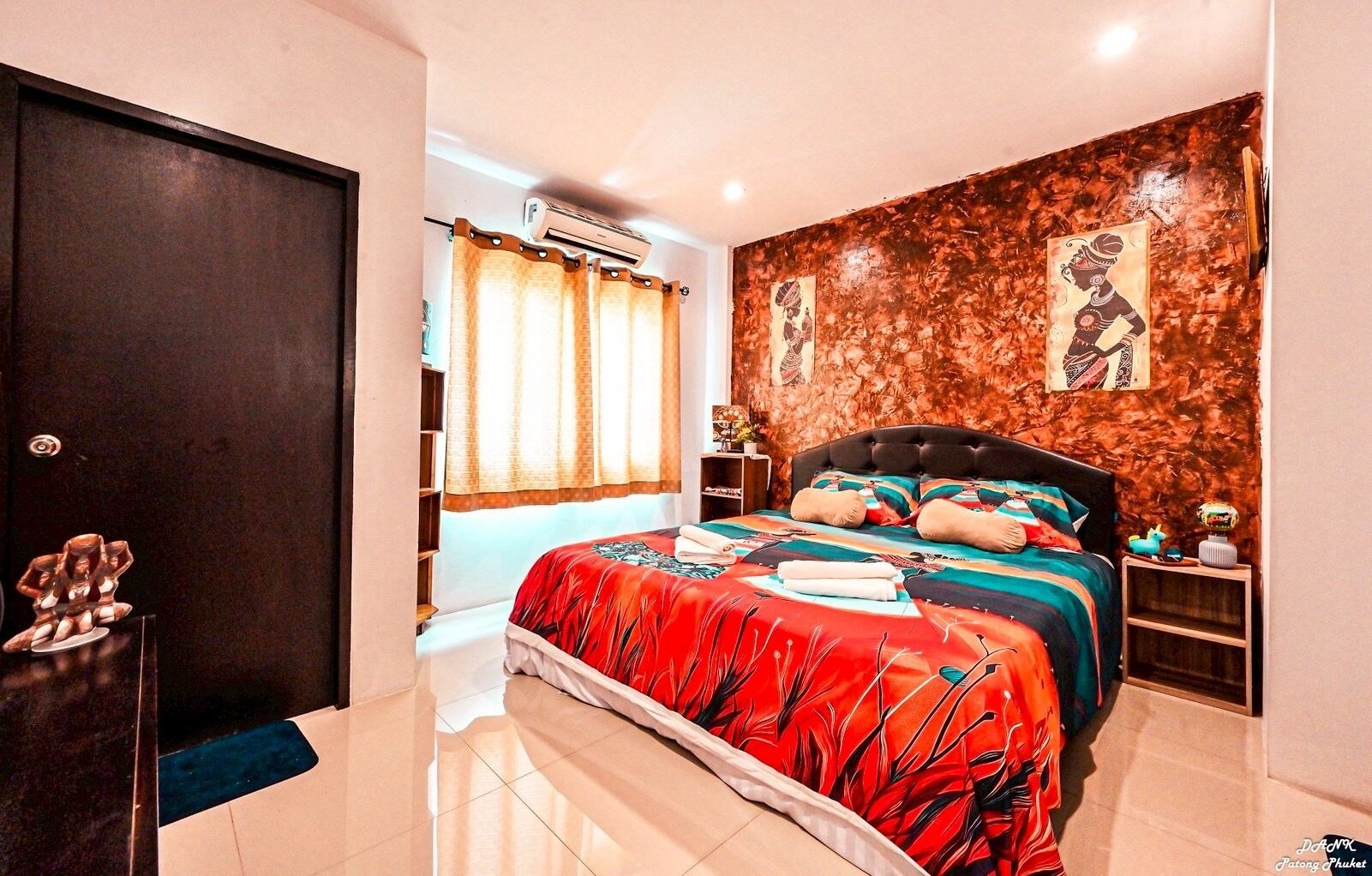 A bedroom with a large bed, a wardrobe, a nightstand, and a wall with artwork.