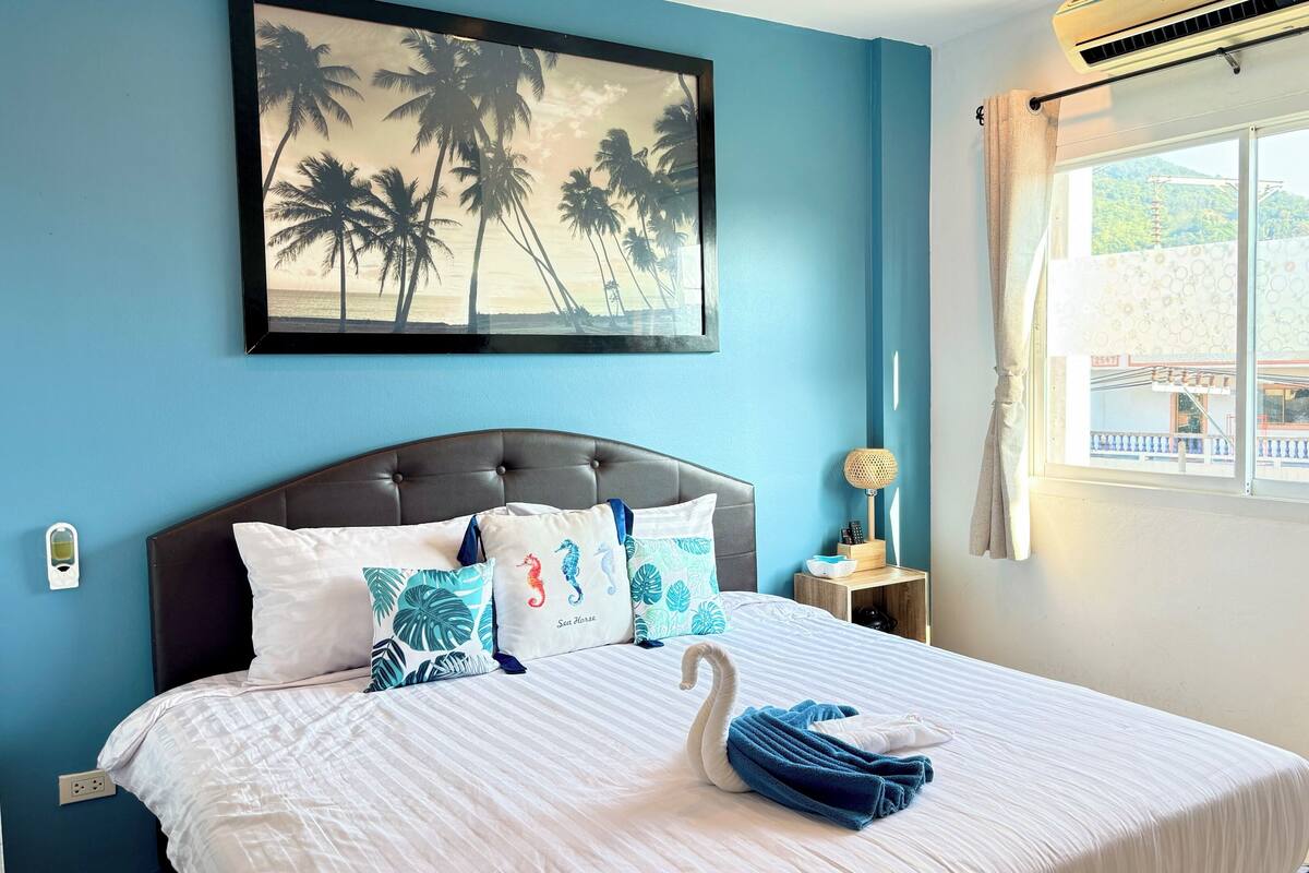 A bedroom with a bed, a nightstand, a wall-mounted air conditioner, and a window with a view.