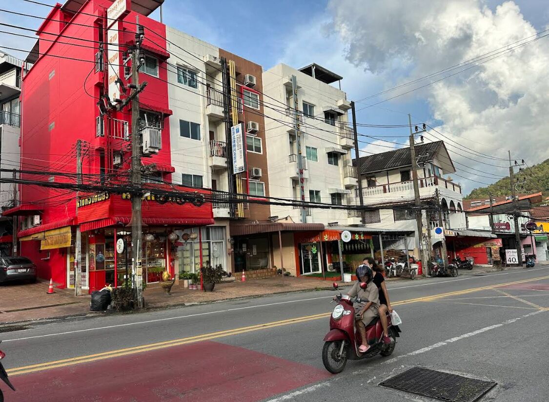 Una calle con un edificio rojo y una motocicleta con dos pasajeros.