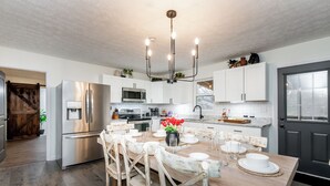 A modern kitchen with stainless steel appliances, a wooden dining table set with white plates and glasses, and a black door with a window.