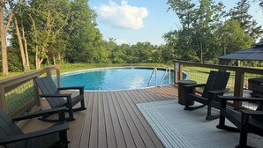 A wooden deck with a pool, surrounded by trees and a clear sky.
