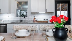 A modern kitchen with white cabinets, a granite countertop, and a dining area with a wooden table set for four.
