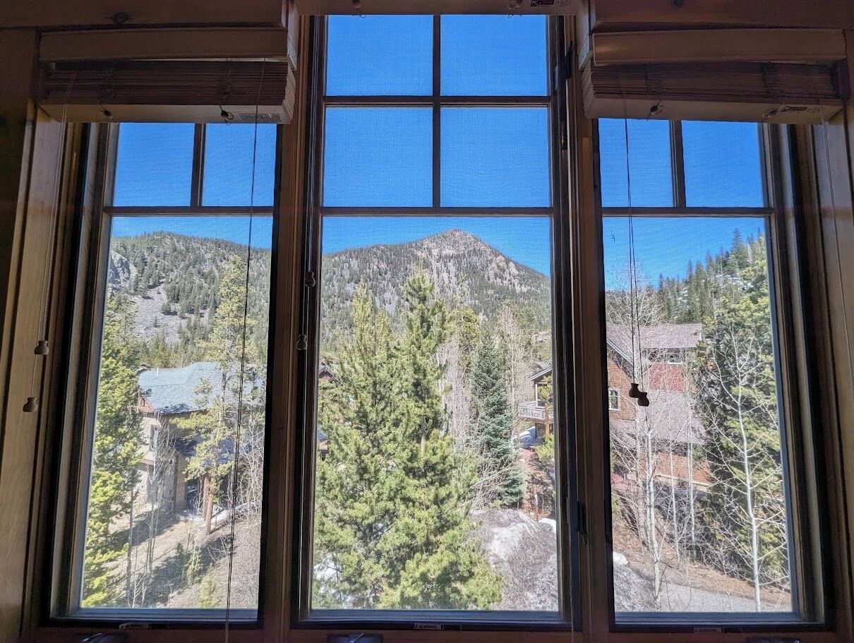 Une pièce dotée d’une grande fenêtre donnant sur un paysage montagneux, avec des arbres et des bâtiments.