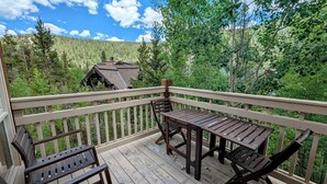 A wooden deck with a table and chairs, surrounded by a railing, overlooking a forested area. - Settlers Creek 6521 (Keystone)