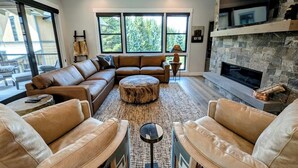A modern living room with a stone fireplace, leather sofas, and large windows offering a view of the outdoors.