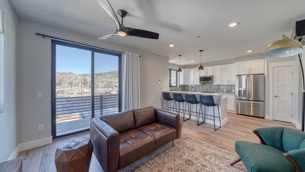 A modern living room with a brown leather sofa, a green armchair, and a large window offering a city view. - Dog Friendly! The Mayfly Hotel, Unit 1C (Salida)