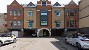 Un immeuble à plusieurs étages doté d’une entrée centrale, de places de stationnement et d’une façade en briques.
