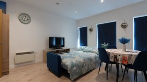 Une chambre à coucher moderne avec un lit, un téléviseur, une table à manger avec des chaises et une horloge au mur.