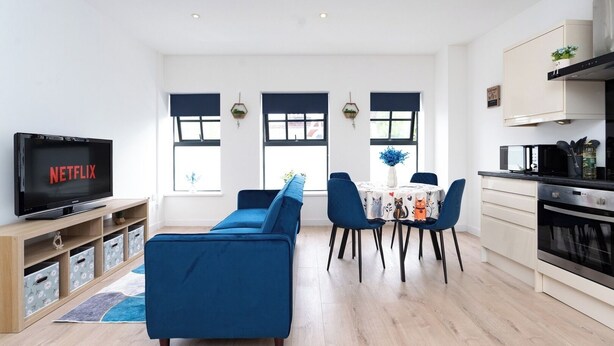 Un salon moderne avec un canapé, un téléviseur affichant le logo « NETFLIX » et un coin repas comprenant des chaises et une table.