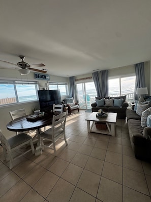 Sala de estar com televisão, mesa de jantar e cadeiras, um sofá e vista para o oceano.