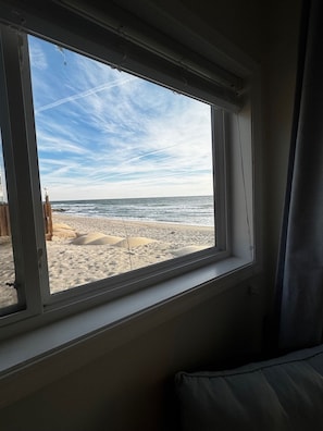 Quarto com janela para uma praia arenosa e o oceano.