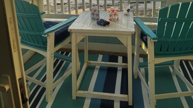 A covered outdoor seating area with two chairs and a table, overlooking the ocean. - Oceanfront Ground Floor End-Unit Condo w/pool -
Shamrock Sands M1 @ The Riggings (Kure Beach)