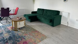 A living room with a green sofa, a red chair, a small round table, and a colorful rug.