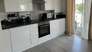 A modern kitchen with white cabinets, a stainless steel range hood, a microwave, a kettle, and a dishwasher.