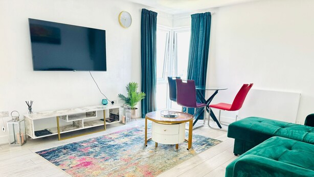 A modern living room with a flat-screen TV, a marble console table, a colorful rug, a green sofa, and a red chair.
