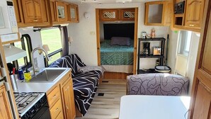 Interior compacto de una caravana con kitchenette, comedor, cama y un pequeño rincón de estar.